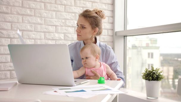 Working mother with baby at table. Working mom with beautiful infant on hands - Photo, Image