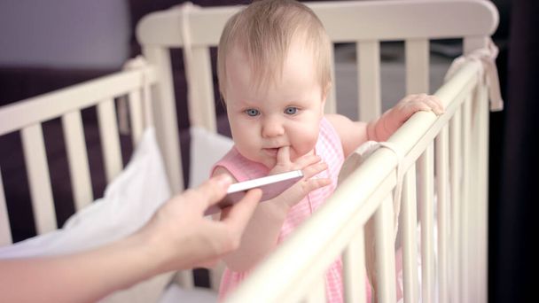 ベビーベッドの幼児の女の子。かわいい赤ちゃんはスマートフォンを探している。幼児-ベッド - 写真・画像