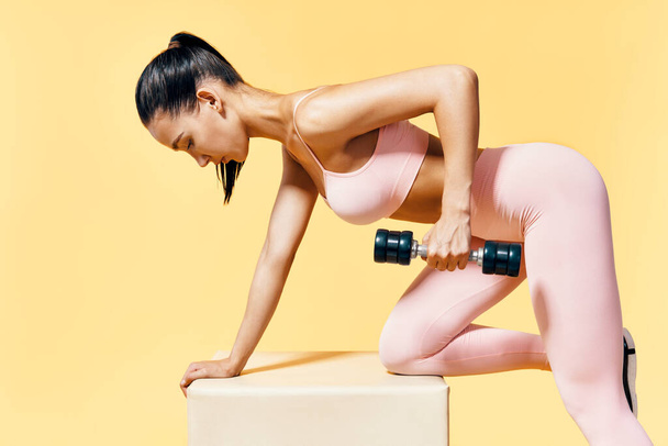 Young sporty woman in sportswear doing exercise with dumbbells on yellow background - Foto, afbeelding