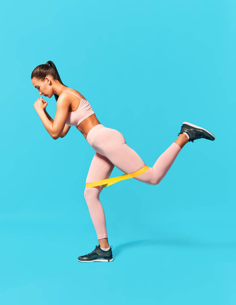 Sporty woman with resistance band loop workouts on blue background - Fotó, kép