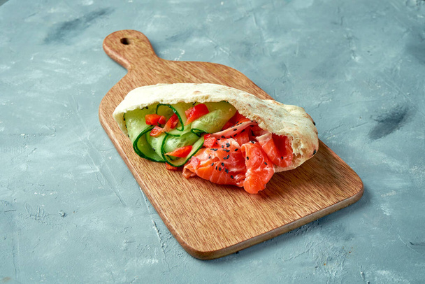Greek pita with salmon and cucumber on a wooden board on a gray background. - Foto, Imagem