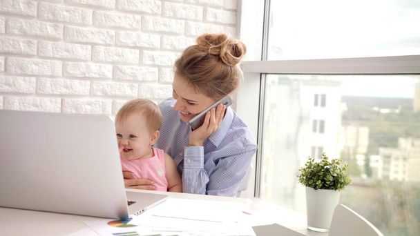 赤ん坊の話す電話を持つ働く女性。子供を持つビジネスママ - 写真・画像
