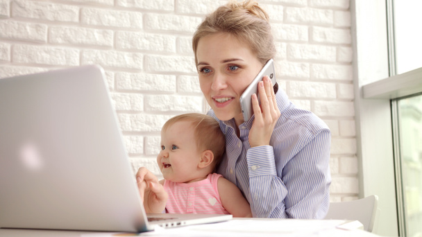 Улыбающаяся женщина с ребенком разговаривает по телефону. Счастливая деловая мать работает на дому - Фото, изображение