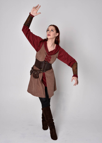 Full length portrait of girl wearing medieval costume. Standing pose holding a sword,  isolated against a grey studio background. - Foto, immagini