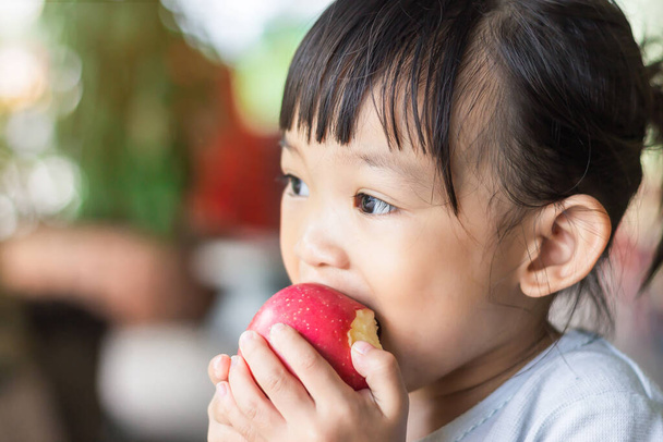 Portrét 2 let starého dítěte. Šťastné asijské dítě dívka jíst a kousat červené jablko. Užij si to. Zdravé jídlo a dětský koncept. Styl ročníku. - Fotografie, Obrázek