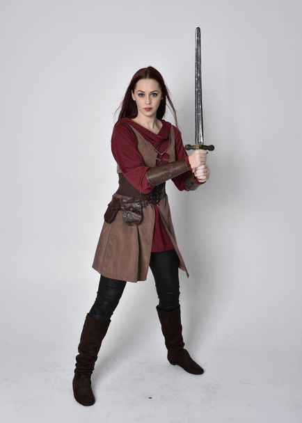 Retrato completo de niña vestida con traje medieval. Posar de pie sosteniendo una espada, aislado sobre un fondo gris estudio. - Foto, Imagen