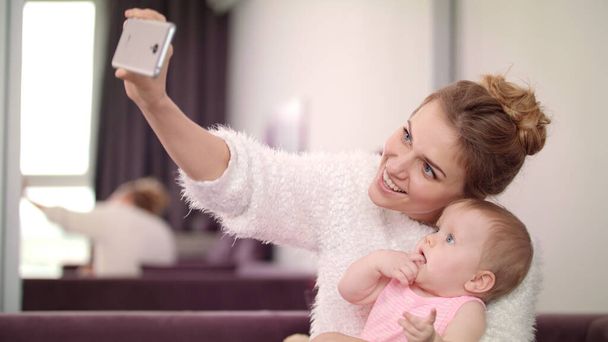 可愛い女が赤ちゃんと自撮り。母親と子供が携帯写真を撮る - 写真・画像