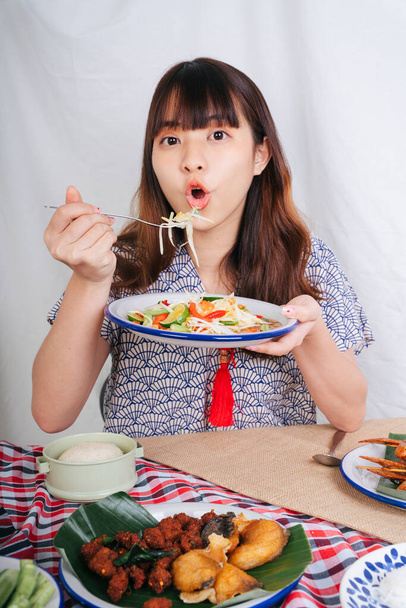 パパイヤサラダを食べる若いアジア人女性の肖像｜島料理とフォーク. - 写真・画像