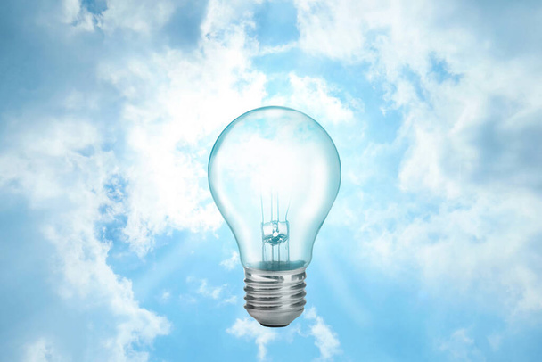 Solar energy concept. Glowing light bulb in sky as sun - Φωτογραφία, εικόνα