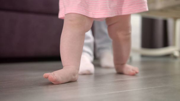Little baby learning walk on floor. Infant doing first steps with father - Photo, Image