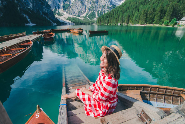 mulher de vestido vermelho sentado em escadas de madeira olhando para o lago nas montanhas. férias de verão - Foto, Imagem