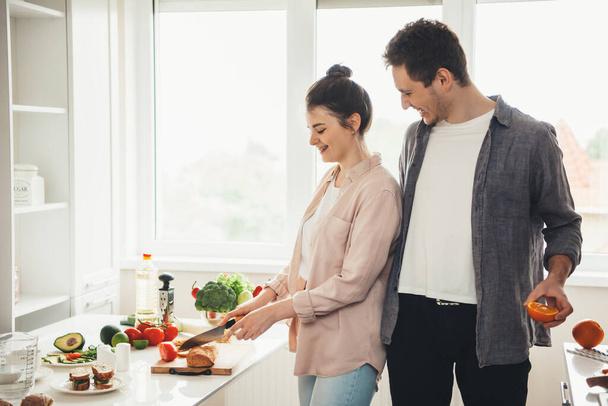 Nuori valkoihoinen pari valmistaa ruokaa yhdessä keittiössä viipaloimalla hedelmiä ja vihanneksia - Valokuva, kuva