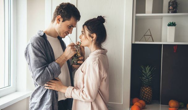 Schönes junges Paar trinkt zu Hause in der Küche einen Mojito und sieht sich an - Foto, Bild