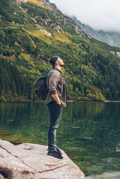hombre sentado en la roca frente al lago en las montañas disfrutando del concepto de senderismo vista - Foto, imagen