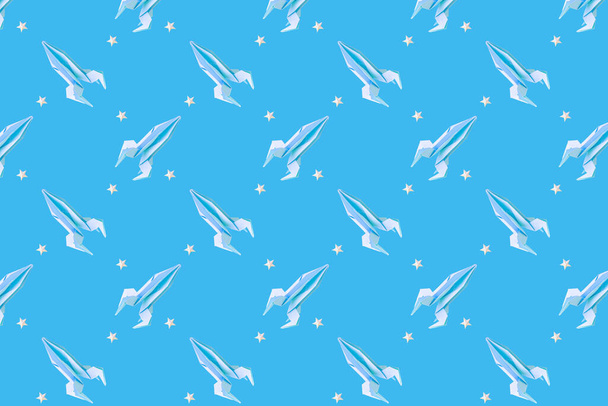 紙の折り紙ロケットは、青い背景、パターン上の紙の星の間を飛ぶ。宇宙の概念。国際人間の宇宙飛行の日、宇宙服の日. - 写真・画像
