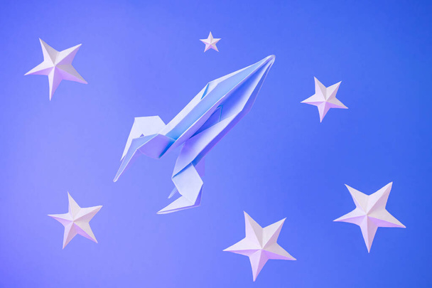 Papier origami fusée vole parmi les étoiles de papier sur un fond bleu. Concept spatial. Journée internationale de l'espace humain Vol, Journée de la cosmonautique. - Photo, image