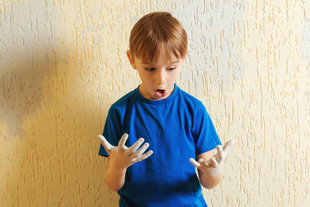 Child with dirty hands from paint. Cute boy having fun during home renovation. Boy making print of his hand on the wall. Kid painting wall at home. - Zdjęcie, obraz