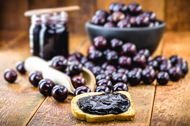 toast with grape jam, on rustic wooden table. Jabuticaba, exotic Brazilian fruit, used in cooking, as a sweet. - Fotografie, Obrázek