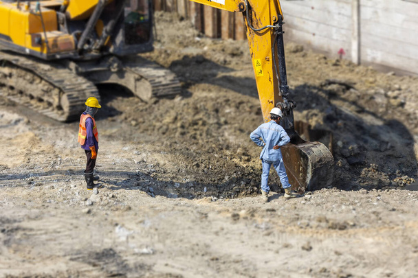 workers wear safety suits with supervisor or engineer see and checking and control excavator backhoe during dig a canal of water drain - Photo, Image