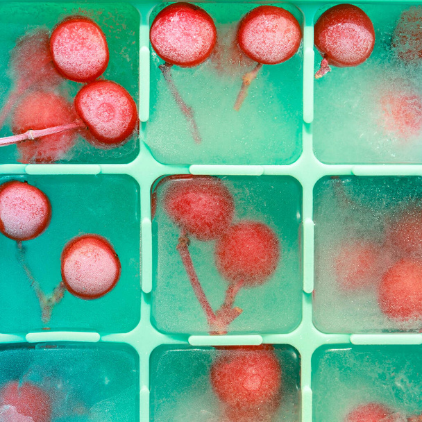 Eis in einer Silikonform für die Tiefkühltruhe in Nahaufnahme. Beeren eingefroren in quadratischen Eiswürfeln - Foto, Bild