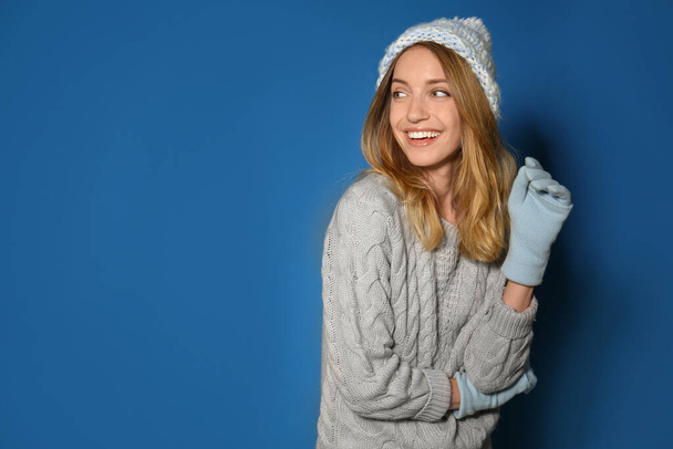 Happy young woman wearing warm sweater, knitted hat and mittens on blue background. Space for text - Фото, зображення
