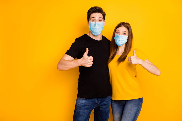 Portrait of his he her she nice attractive healthy couple showing thumbup wearing safety mask stop pandemia mers cov influenza prevention isolated vibrant yellow color background - Fotoğraf, Görsel