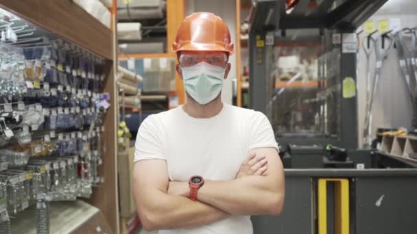 Fehér ipari munkás narancssárga keménykalapban, védőszemüvegben és orvosi maszkban a barkácsboltban, egy rakományemelő mögött. Férfi raktár munkás maszk coronavirus, covid 19 - Felvétel, videó