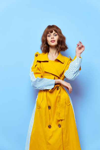 Fashionable woman in coat on blue background holds hand at waist  - Photo, Image