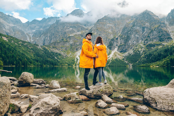 homme avec femme en imperméable jaune à la journée ensoleillée d'automne en regardant le lac dans les montagnes tatra concept de randonnée - Photo, image