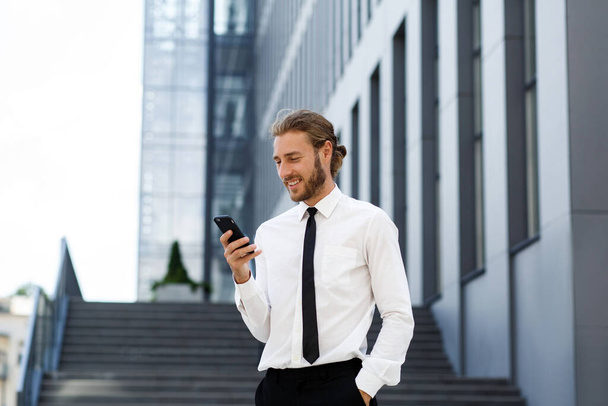 Portrait of a successful young businessman. A curly-haired man in a white shirt with a telephone against the background of a modern business center - Foto, afbeelding