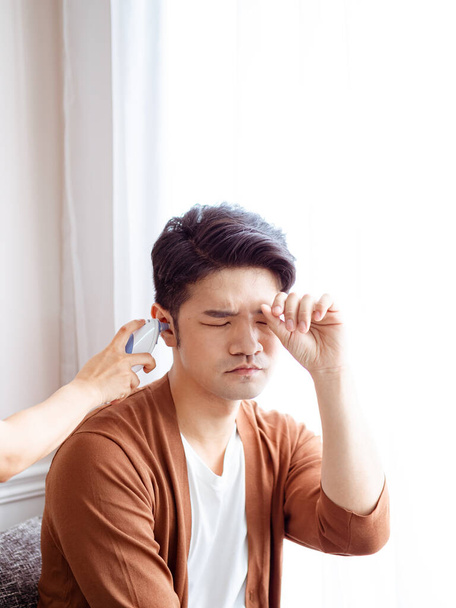 Fiatal ázsiai férfi sebészeti maszkot visel és fülhőmérőt használ - Fotó, kép