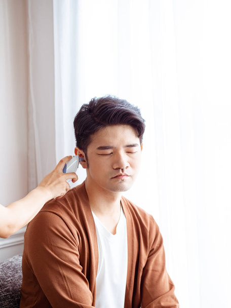 Giovane asiatico uomo indossare chirurgico maschera e utilizzando orecchio termometro - Foto, immagini