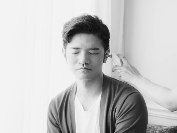 Fiatal ázsiai férfi sebészeti maszkot visel és fülhőmérőt használ - Fotó, kép