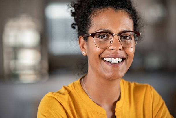Portrait of african woman wearing eyeglasses and relaxing at home. Successful black girl with spectacles looking at camera. Satisfied young mixed race woman sitting on sofa with copy space.  - Fotó, kép