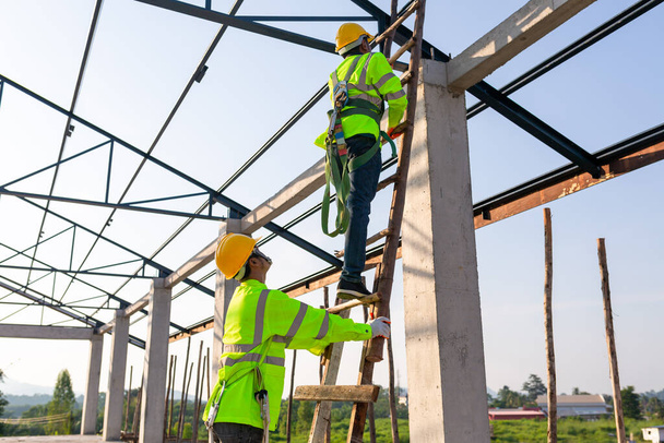 建設現場の安全高さ機器。アジアの労働者は屋根を設置するために安全高さ機器を着用しています。安全ボディハーネス用フック付き作業者用の落下防止装置. - 写真・画像