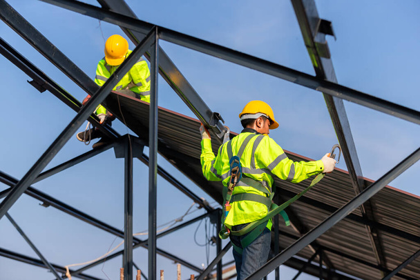 Asiatische Dachbauarbeiter tragen Sicherheitshöhen-Ausrüstung, um den Dachstuhl zu installieren, Fallschutzvorrichtung für Arbeiter mit Haken für Sicherheitsgurt auf der Baustelle. - Foto, Bild