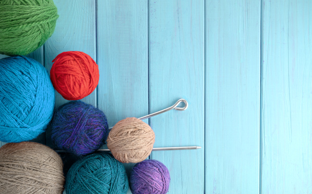 Palle di filato in diversi colori con ferri da maglia su uno sfondo di texture di legno blu. - Foto, immagini