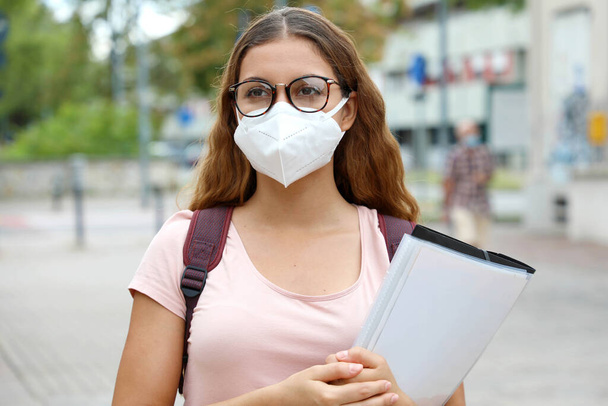 COVID-19 Όμορφη μαθήτρια με προστατευτική μάσκα περπατώντας στο δρόμο της πόλης. Κολεγιακή νεαρή γυναίκα πίσω στο σχολείο μετά από πανδημία coronavirus. - Φωτογραφία, εικόνα