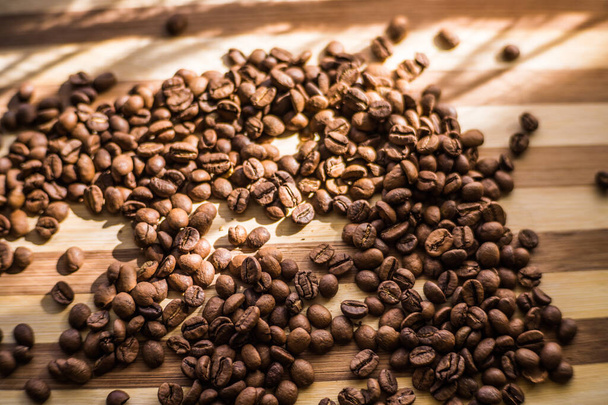 Geröstete Arabica-Kaffeebohnen liegen auf einer Holzplanke verstreut. - Foto, Bild