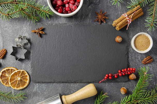 Culinary background with christmas winter spices and ingredients for baking on dark stone table with a black slate with chalkboard for your text. Top view. Copy space.  - Foto, immagini