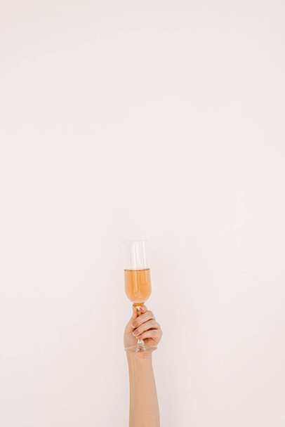 Egészségetekre! Női kéz egy pohár rózsa pezsgőt tartva a fehér falnak. Boldog születésnapot, évfordulós party ünneplő dekoráció ünnepi koncepció - Fotó, kép