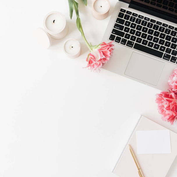 Laptop en mooie roze pioenroos tulp bloemen, blanco vel papier kaart, kaarsen op witte achtergrond. Flat lay, bovenaanzicht minimalistisch thuiskantoor werkruimte met blanco kopieerruimte - Foto, afbeelding