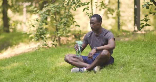Nuori afrikkalainen amerikkalainen kaveri juo vettä urheilupullosta - Materiaali, video