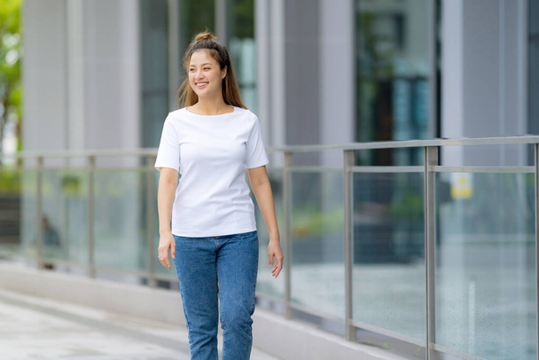 フロントビュー、白いTシャツと青いジーンズの女性は、街の通りの背景、夏の日の外に立って - 写真・画像