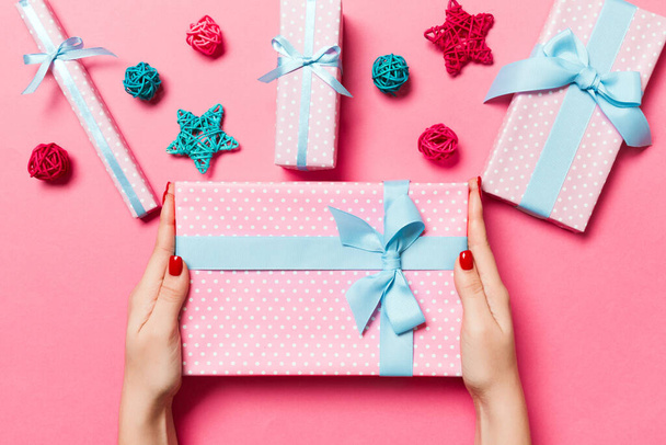 Draufsicht weiblicher Hände mit einem Weihnachtsgeschenk auf festlichem rosa Hintergrund. Weihnachtsdekoration, Spielzeug und Bälle. Neujahrsferien-Konzept. - Foto, Bild