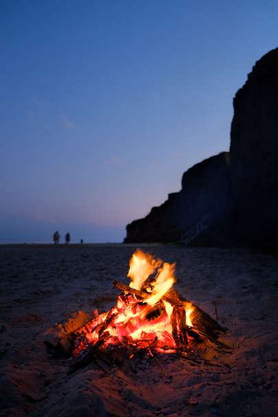 Fuego ardiendo en la costa de arena en una soleada noche de verano. Pequeño fuego arde dentro de una chimenea en la playa vacía al atardecer magnífico. - Foto, imagen