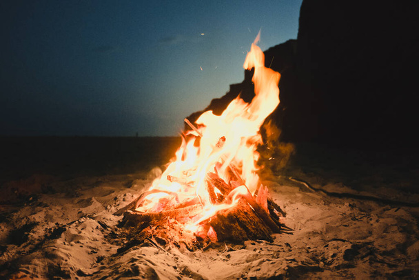 Огонь горит на песчаном побережье солнечным летним вечером. Маленький огонь горит внутри камина на пустом пляже. Фото с эффектом пленки и зерна - Фото, изображение