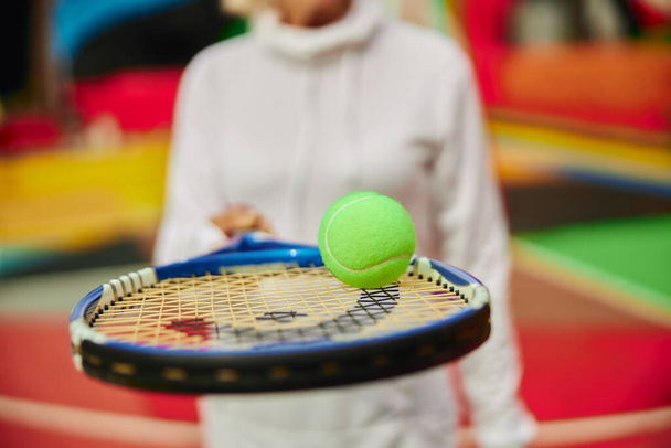 Vieille dame saine et gaie sur une place pleine de couleurs à l'extérieur et tenant une raquette de tennis avec balle - Photo, image