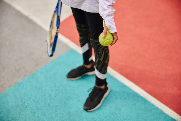 Yaşlı, sağlıklı ve neşeli bir bayan açık meydanda renkli bir meydanda ve elinde topla tenis raketi tutuyor. - Fotoğraf, Görsel