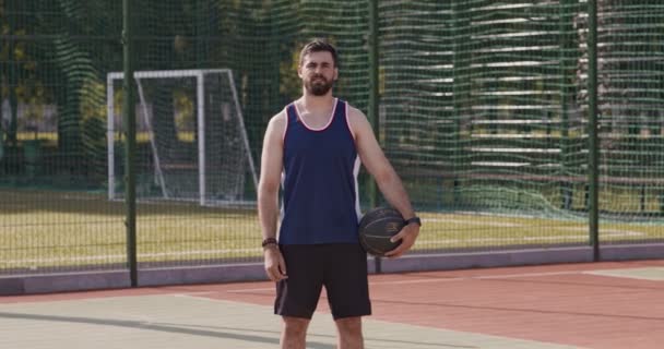 Стритболист, стоящий с баскетбольным мячом на открытой площадке - Кадры, видео